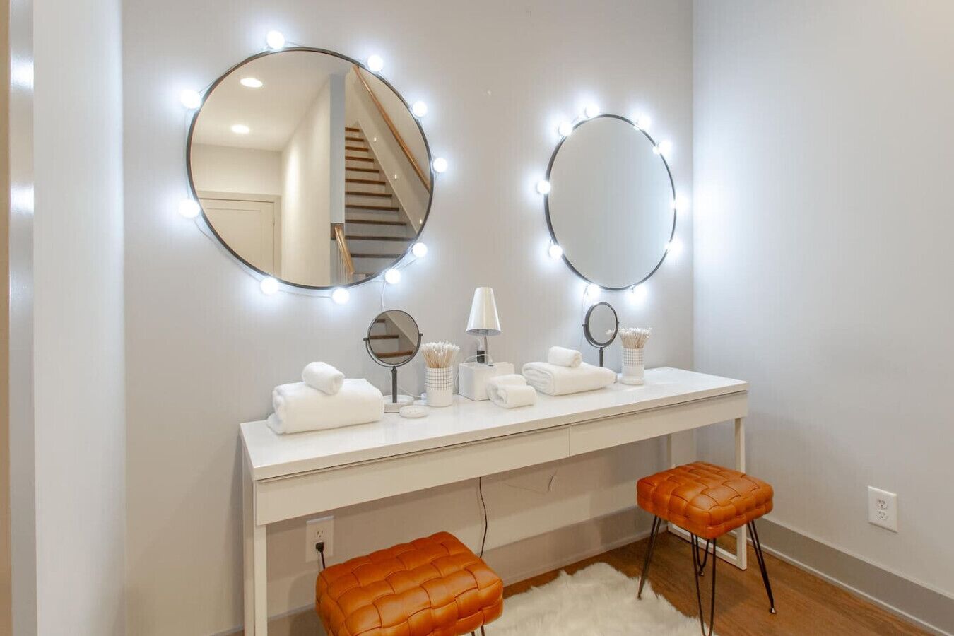 A vanity area with a white vanity, two mirrors, and a stool.