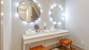 A vanity area with a white vanity, two mirrors, and a stool.