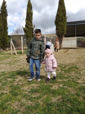 Children can play freely in the grassy area surrounded by a fence and trees.