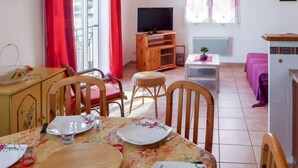 Ein Essbereich mit Tisch für zwei Personen, einem Fernseher und einem kleinen Tisch mit Pflanze.
