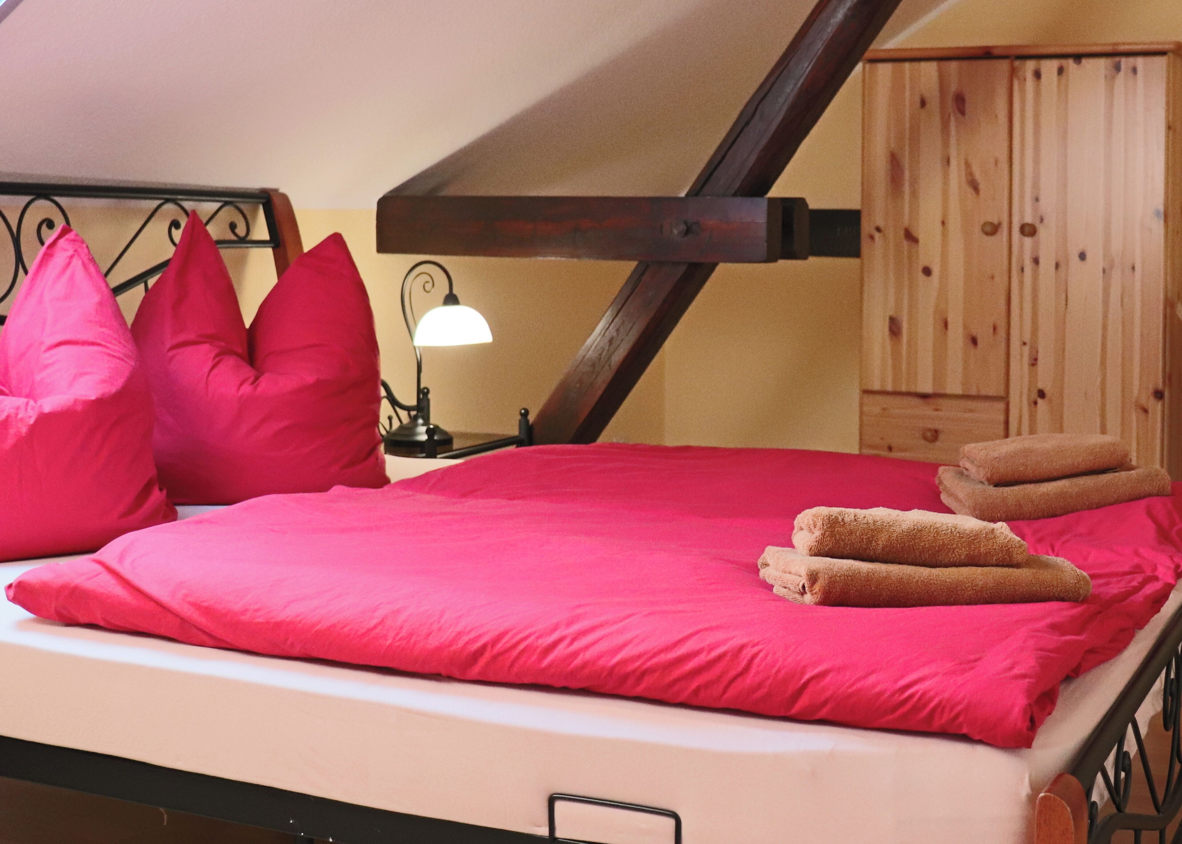 Una cama con ropa de cama rojo intenso, una lámpara en una mesita de noche y muebles de madera.