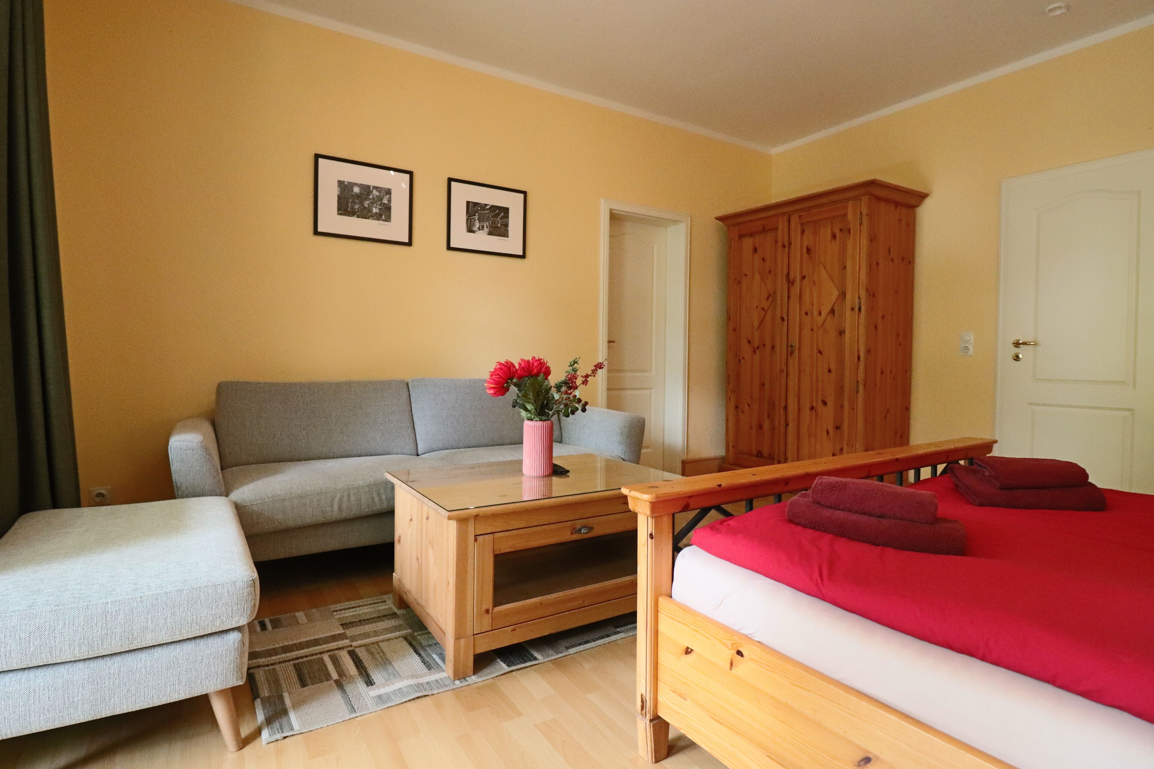 Una habitación con una cama, un sofá, un armario de madera y dos cuadros en la pared.