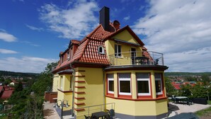 A yellow building with a red-tiled roof, a balcony, and a view of the surrounding area. - Villa Am Ehrensteig (Eisenach)