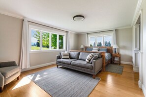 Ein Wohnzimmer mit einer Couch, einem Couchtisch, einem Teppich und Blick auf eine grüne Landschaft durch große Fenster.
