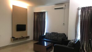A living room with a flat-screen TV mounted on a wooden panel, a sofa, a coffee table, and a TV stand. - De' Viana Hotel & Apartment (Kota Bharu)