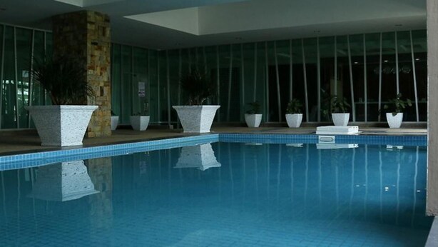 An indoor swimming pool with clear blue water, surrounded by large windows and potted plants. - De' Viana Hotel & Apartment (Kota Bharu)
