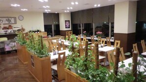 Un restaurant avec des chaises et des tables en bois, des plantes en pot et une horloge au mur.