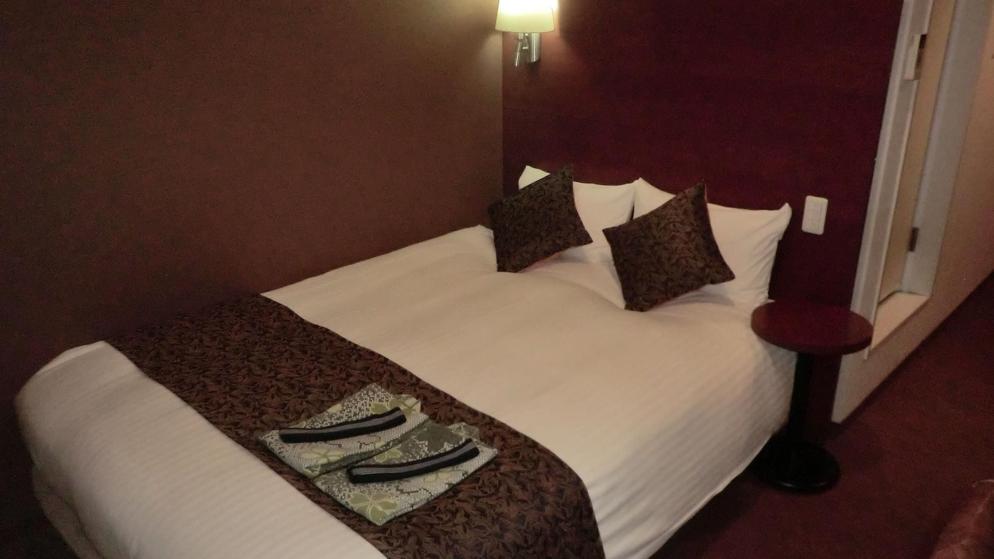 A hotel room with a bed, a nightstand, and a wall-mounted lamp.