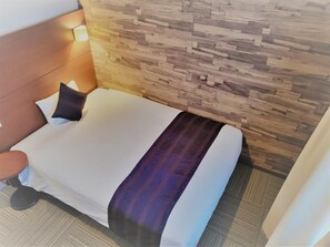 A hotel room with a bed, a headboard, a bedside table, and a wall with a wooden pattern.