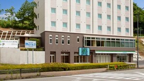 Un edificio de varios pisos con un letrero verde y blanco en la parte superior, un cartel de estacionamiento y un cielo azul despejado.