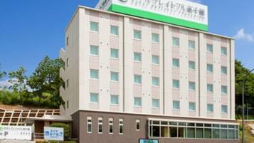 A multi-story building with a green and white sign on top, a parking sign, and a clear blue sky.