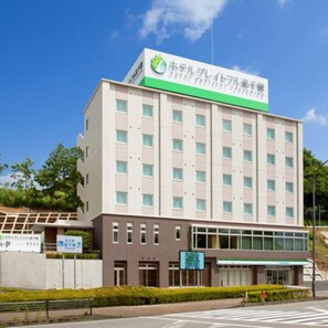 Un edificio de varios pisos con un letrero verde y blanco en la parte superior, un cartel de estacionamiento y un cielo azul despejado.
