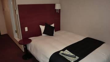 A hotel room with a large bed, a round bedside table, a red headboard, and a wall-mounted lamp.