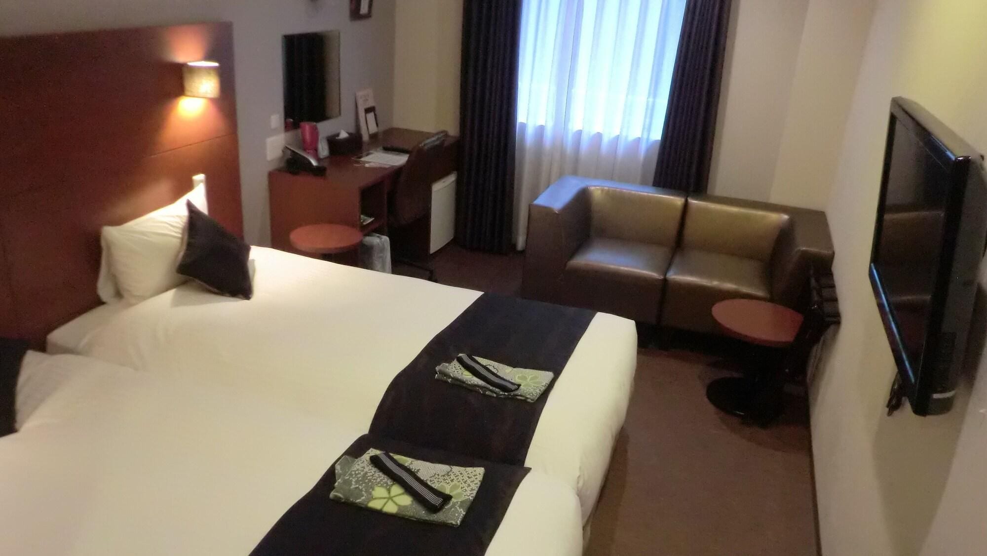 A hotel room with a large bed, a desk, a sofa, a TV, and a window with curtains.