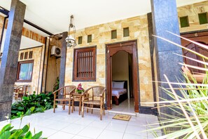 A hotel entrance with a covered patio area, wooden furniture, and a bed visible inside. - Teba House Bisma Ubud by Ecommerceloka (Ubud)