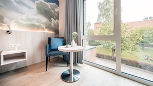 A modern room with a large window, a round table with a vase, a blue chair, and a wall-mounted shelf.