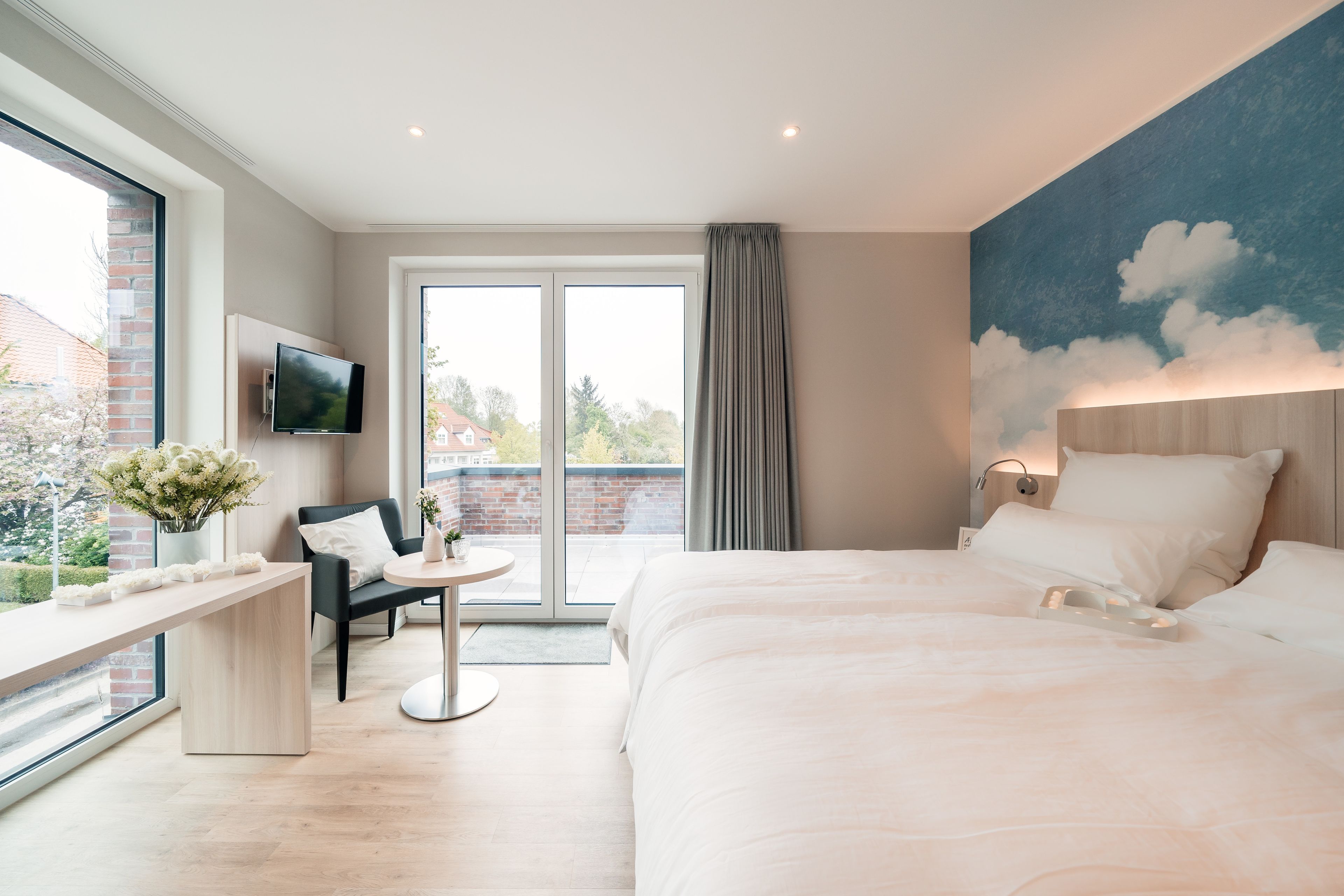 Habitación de hotel moderna con una cama grande, un escritorio con silla, un televisor montado en la pared y un amplio ventanal con vistas al exterior.