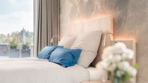 A modern bedroom with a large bed, two bedside lamps, and a view of the outdoors.