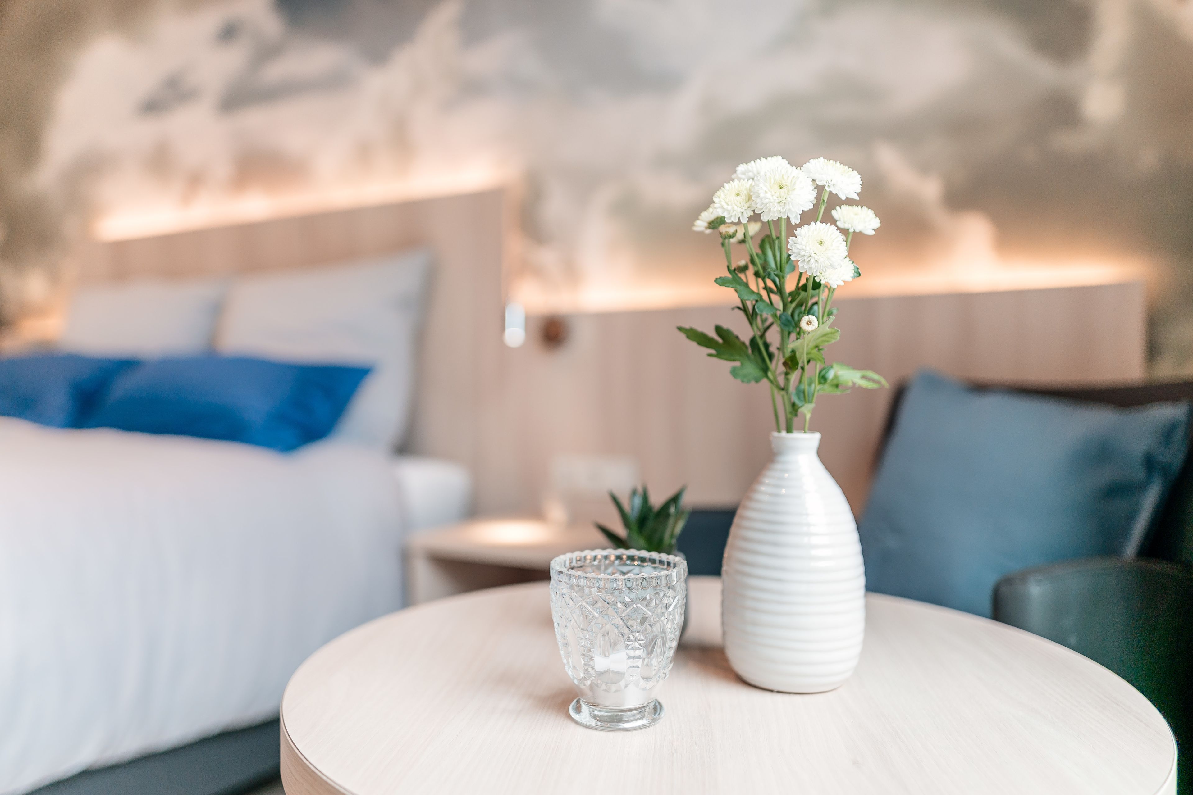 Ein Schlafzimmer mit einem Bett, einem Nachttisch, einer Vase mit Blumen und einer Lampe.