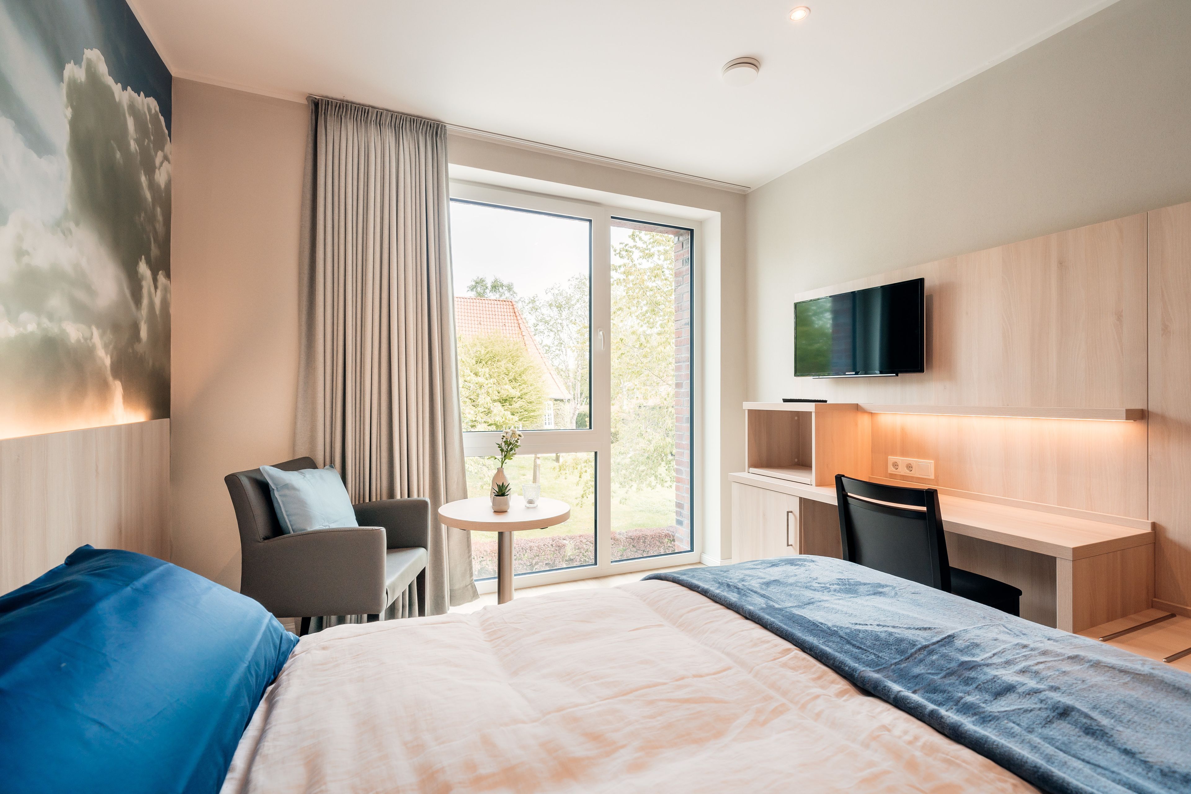 Una habitación de hotel moderna con una cama grande, un escritorio, una silla, un televisor y una ventana con cortinas.