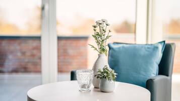 A round table with a vase of flowers and a glass on it, placed in front of a window with a brick wall in the background.