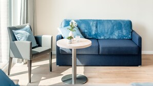 A modern living room with a blue sofa, a round table with a vase and a glass, and a grey armchair.