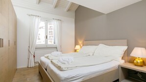 Een slaapkamer met een bed, bedlampen, een raam met gordijnen en een houten garderobe.