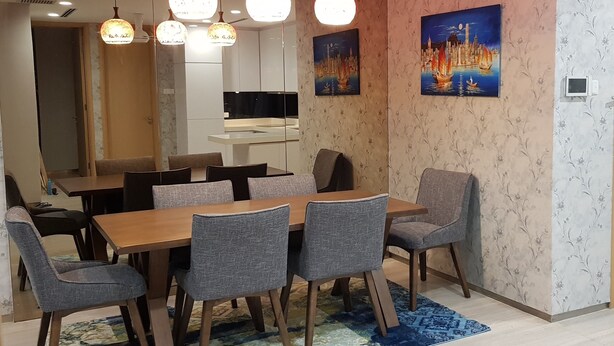 En matplats med ett träbord och grå klädda stolar, en stor målning som föreställer en stadsbild och hängande, sfäriska lampor.