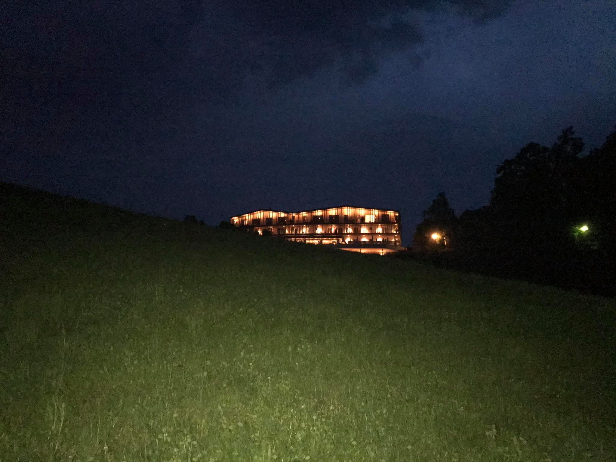 Ein modernes Gebäude mit mehreren beleuchteten Stockwerken, gelegen auf einem grasbewachsen Hügel.