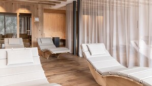 Un cuarto de spa con suelo de madera, varios sillones de sol, una pared de madera y un ventanal con cortinas translúcidas.