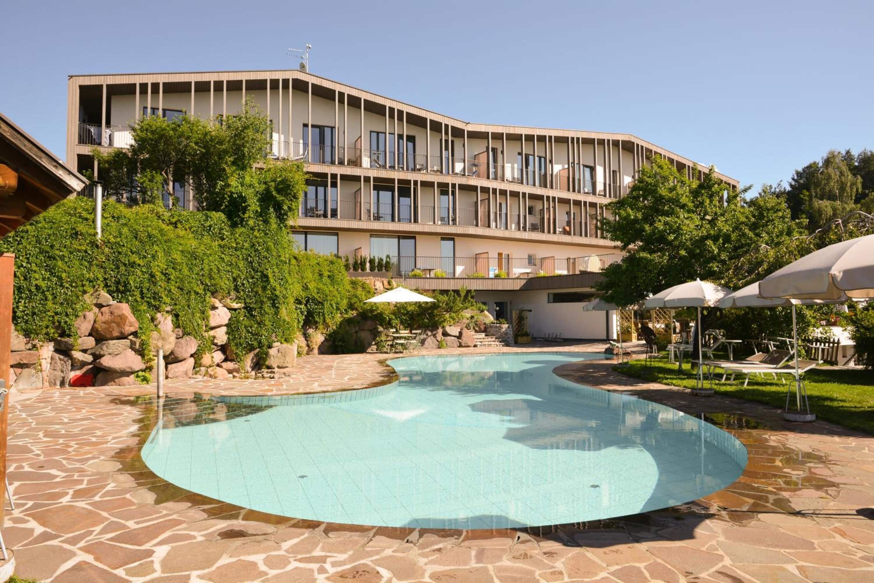A modern hotel with a swimming pool, outdoor seating, and a landscaped garden.