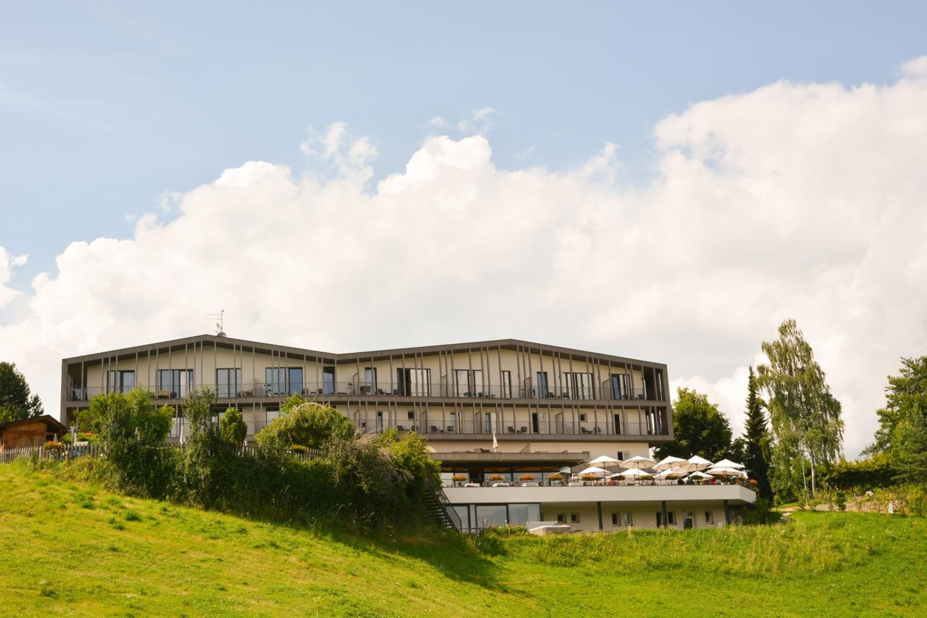 Un hotel de varios pisos con techo plano, balcones y área de estar al aire libre con sombrillas.