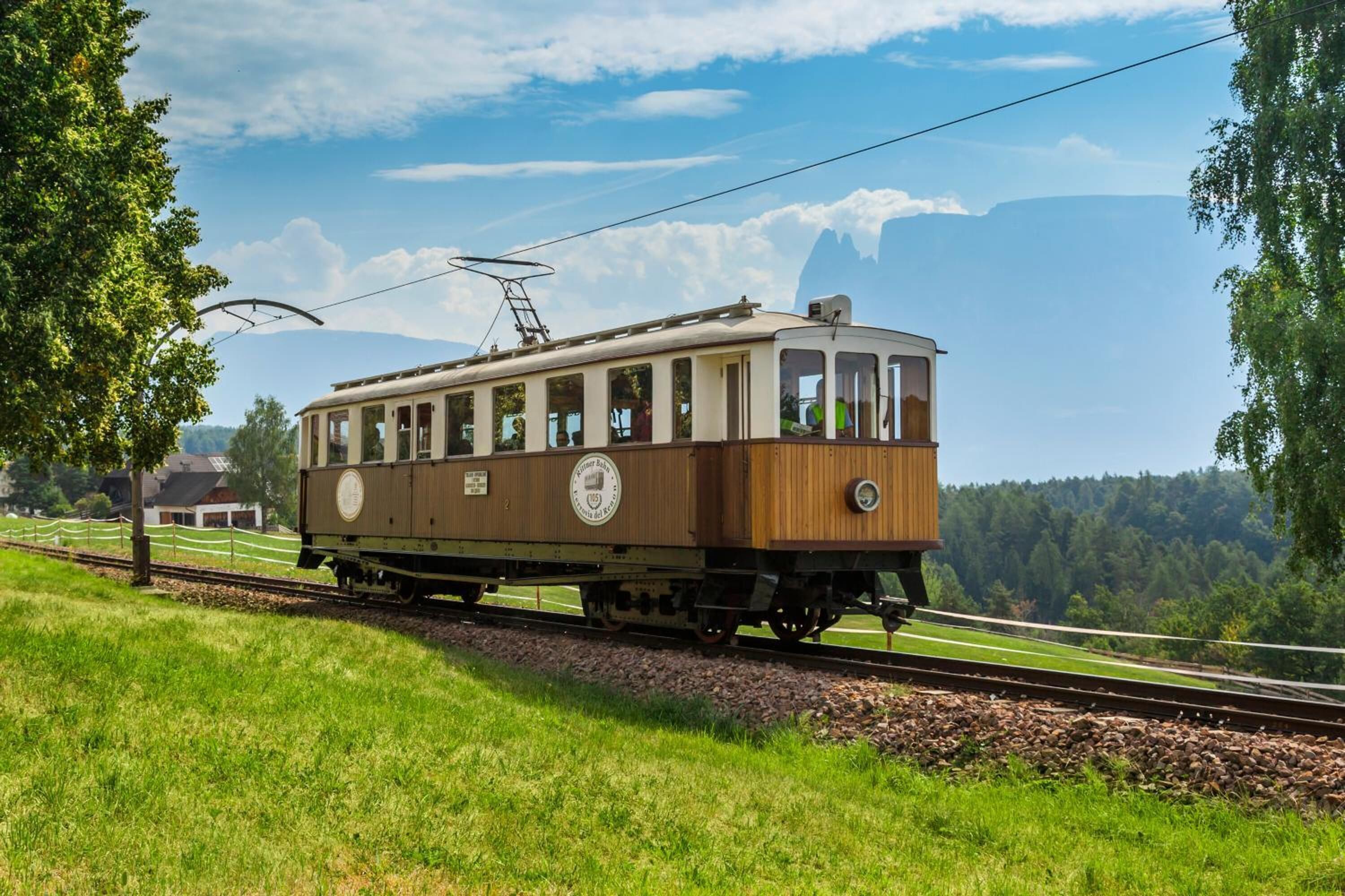 Un tram storico su un binario circondato da vegetazione e un cielo sereno.
