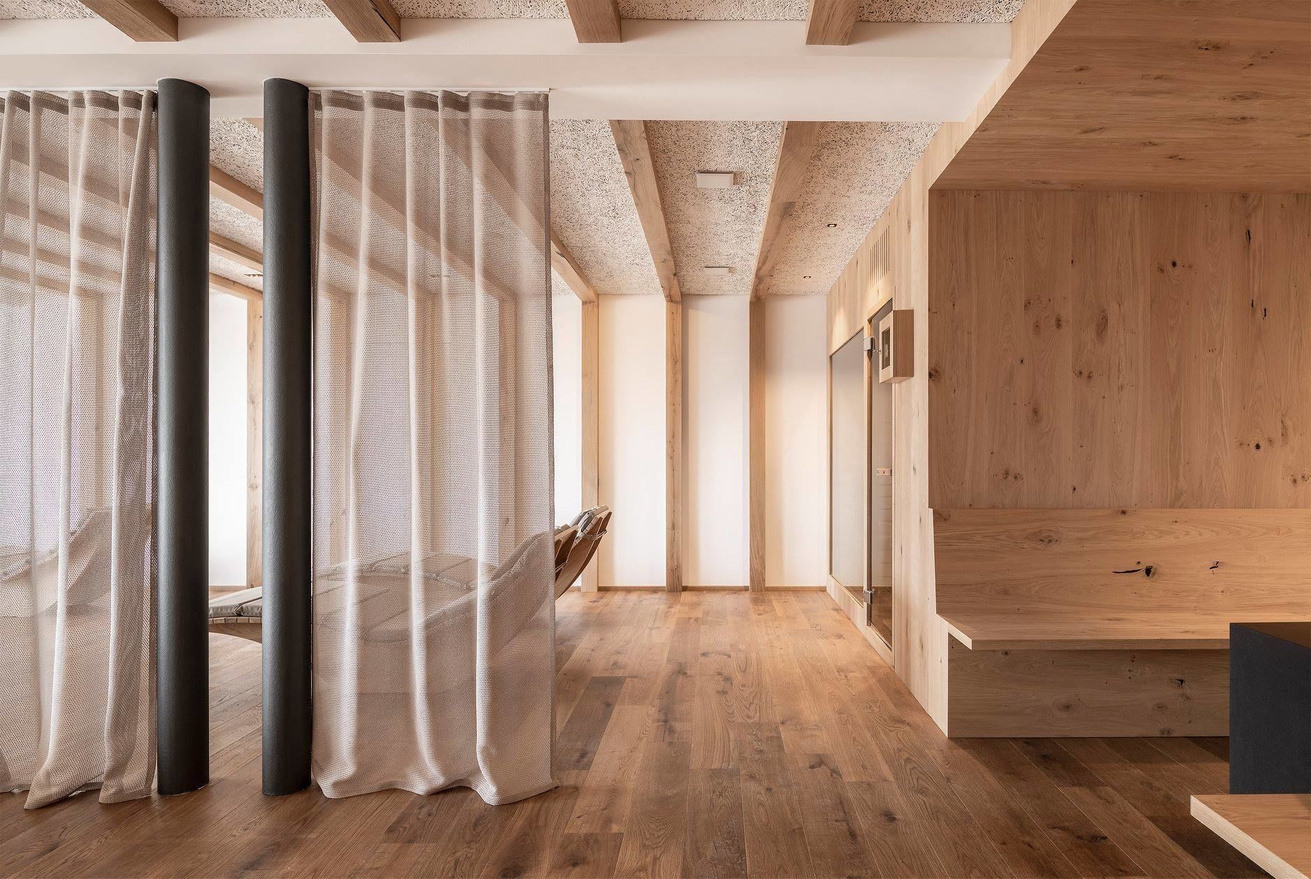 A modern interior with wooden flooring, a high ceiling with exposed beams, and a large window with sheer curtains.