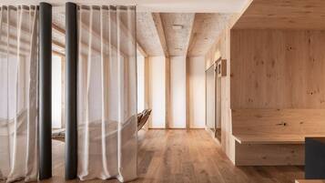 Un interior moderno con suelo de madera, un techo alto con vigas a la vista y un gran ventanal con cortinas traslúcidas.