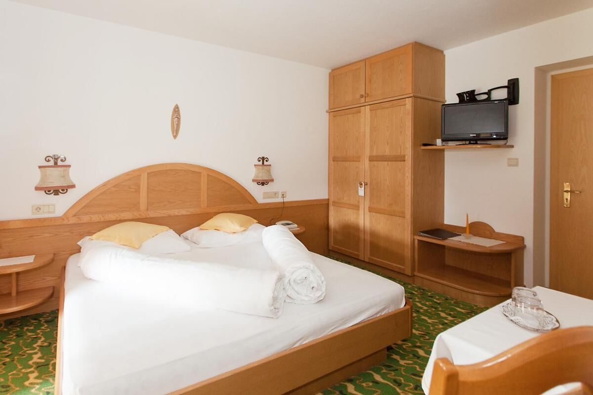 Camera d'albergo con un letto in legno, una televisione su una mensola, una scrivania con una sedia e un armadio.