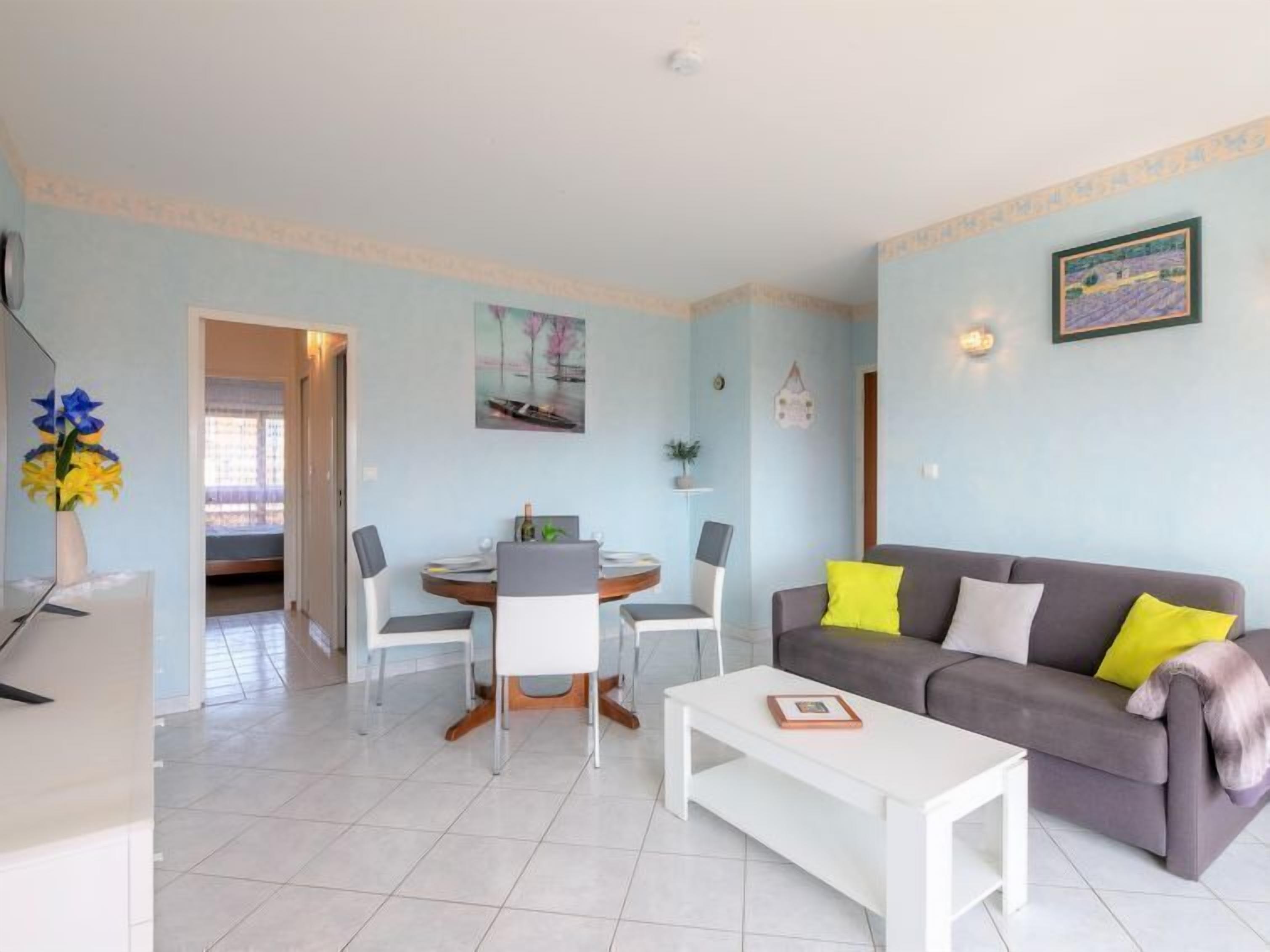 A living room with a grey sofa, white coffee table, and a dining area with a table and chairs.