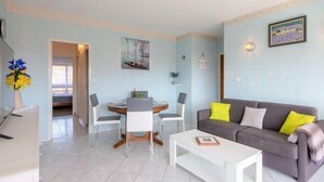 A living room with a grey sofa, white coffee table, and a dining area with a table and chairs. - Le Maxime by Interhome (Sainte Maxime)