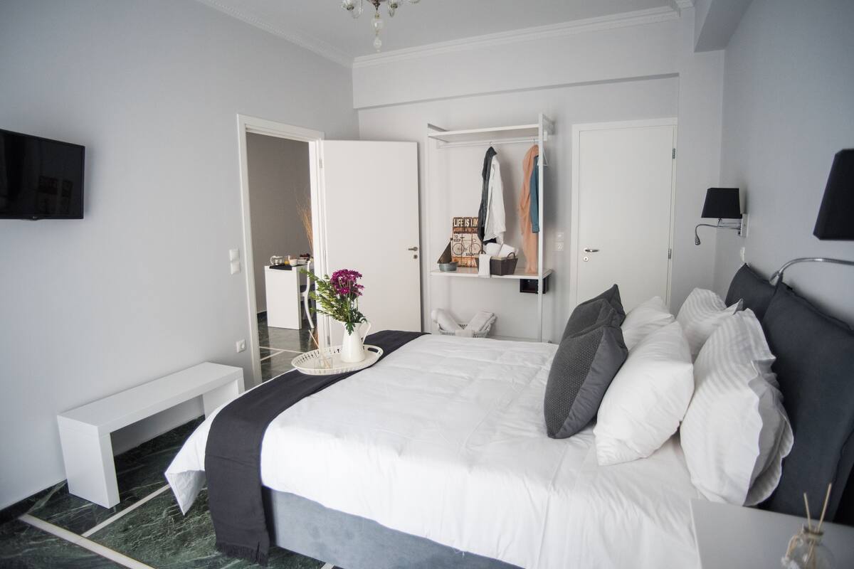 A modern hotel room with a large bed, a bedside table, a bench, a wardrobe, and a television.