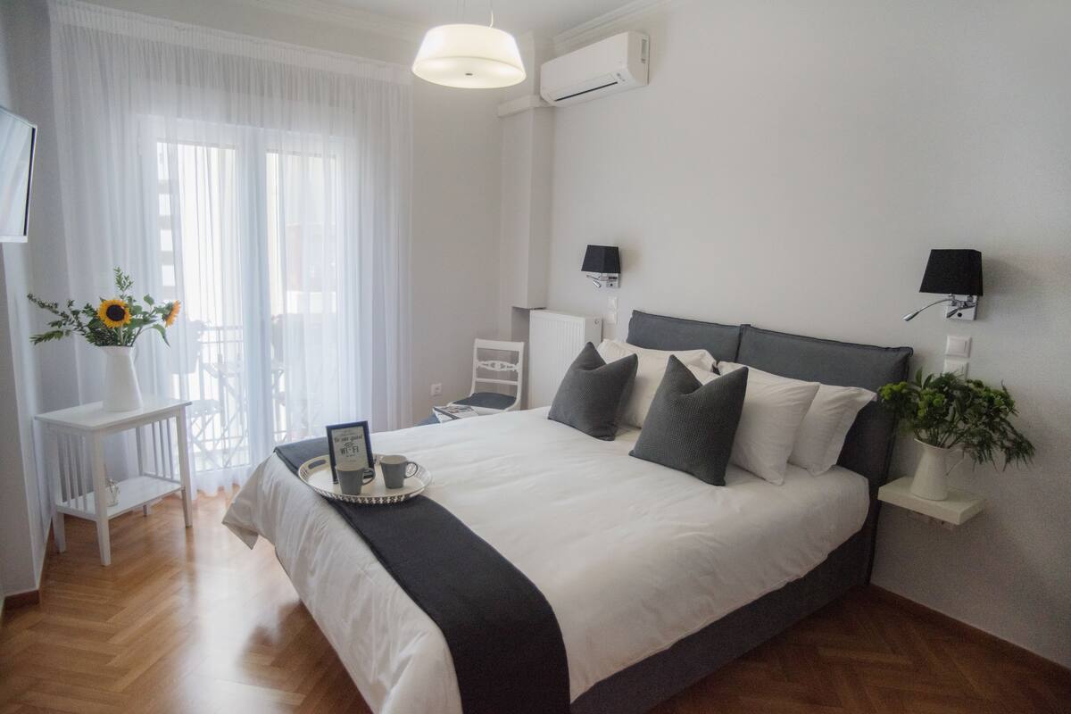 A neatly arranged bedroom with a large bed, bedside lamps, a small table with a tray, and a potted plant.