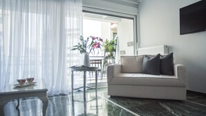 Ein modernes Wohnzimmer mit Marmorboden, einer weißen Couch mit grauen Kissen, einem kleinen Tisch mit einer Teetasse und durchsichtigen Vorhängen.