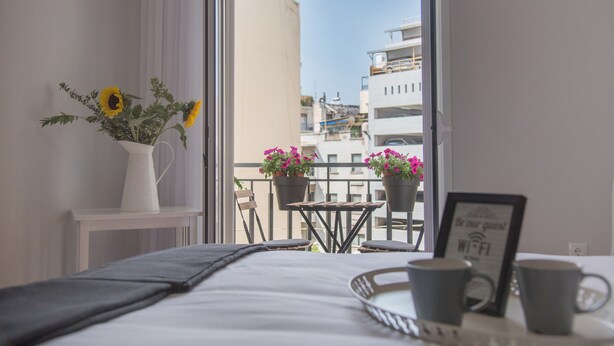 Ein Hotelzimmer mit einem Bett, einem kleinen Tisch mit zwei Stühlen, einer Vase mit Sonnenblumen und einem Balkon mit Topfpflanzen und einem Schild für WLAN.