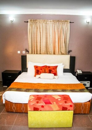 A neatly made bed with a patterned bedspread, a pillow, and a matching ottoman. - Suru Express Hotel Surulere (Lagos)