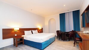 Une chambre d’hôtel comprenant un lit, des tables de chevet, un bureau avec une chaise et un grand miroir.