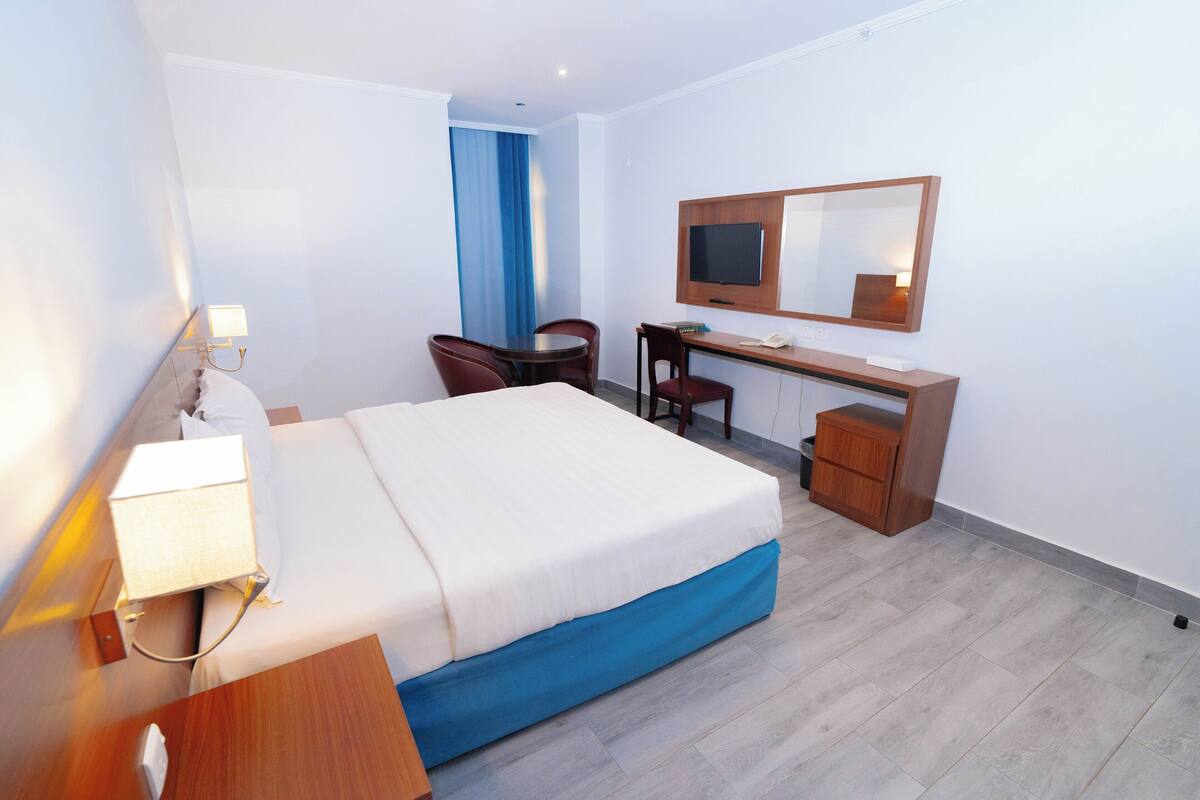 A hotel room with a bed, desk, chair, and a television.