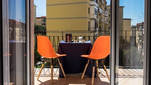 A balcony with two orange chairs and a table set for two, overlooking a cityscape. - Montedonzelli B&B (Naples)