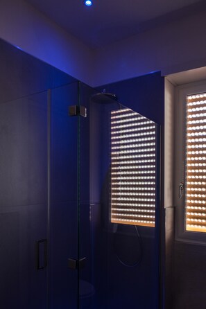 Une salle de bain moderne dotée d’une cabine de douche en verre, d’un pommeau de douche apparent et d’une porte avec une fenêtre.