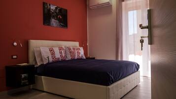 A bedroom with a bed, a nightstand, a wall-mounted air conditioner, and a painting.