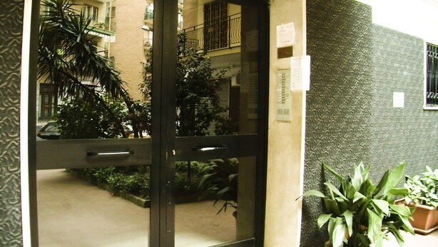 A hotel entrance with a glass door, a small outdoor area with plants, and a textured wall. - Montedonzelli B&B (Naples)