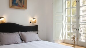 A bedroom with a large bed, two bedside lamps, a painting on the wall, and a window with a decorative door. - APARTMENT OF STANDING THE GENIS (Sarlat-la-Canéda)